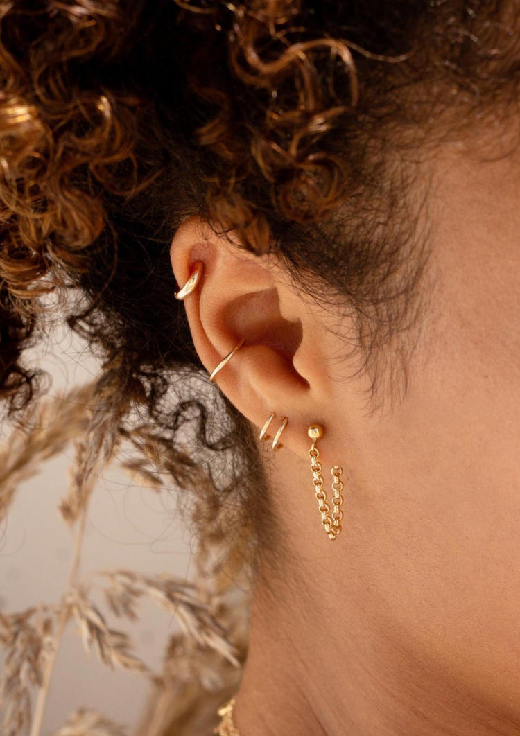 A gold earring stack with a twist earring, a dangly earring as a chain earrings design, and two ear cuffs in the Ear Cuff duo style by Hello Adorn.