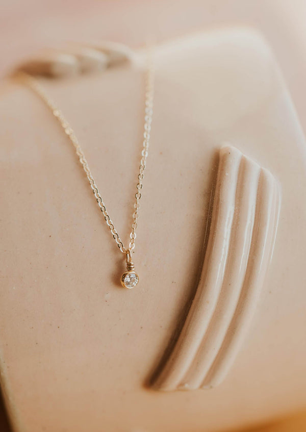 A minimalist necklace from Hello Adorn featuring a stone necklace with a bezel setting necklace diamond hung from a delicate gold chain necklace in the Solitaire Necklace design.
