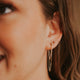 A simple earring stack style by Hello Adorn with a gold dangle earrings as the gold statement earrings paired with a ball stud earring and small gold hoop earrings.