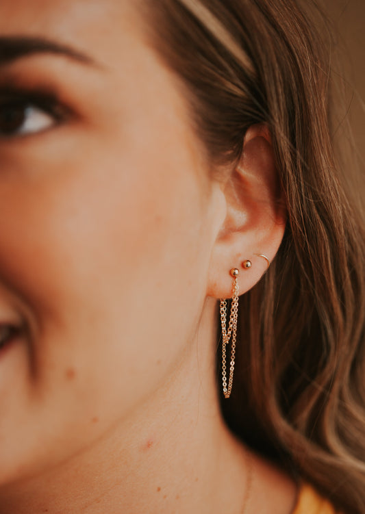 A simple earring stack style by Hello Adorn with a gold dangle earrings as the gold statement earrings paired with a ball stud earring and small gold hoop earrings.