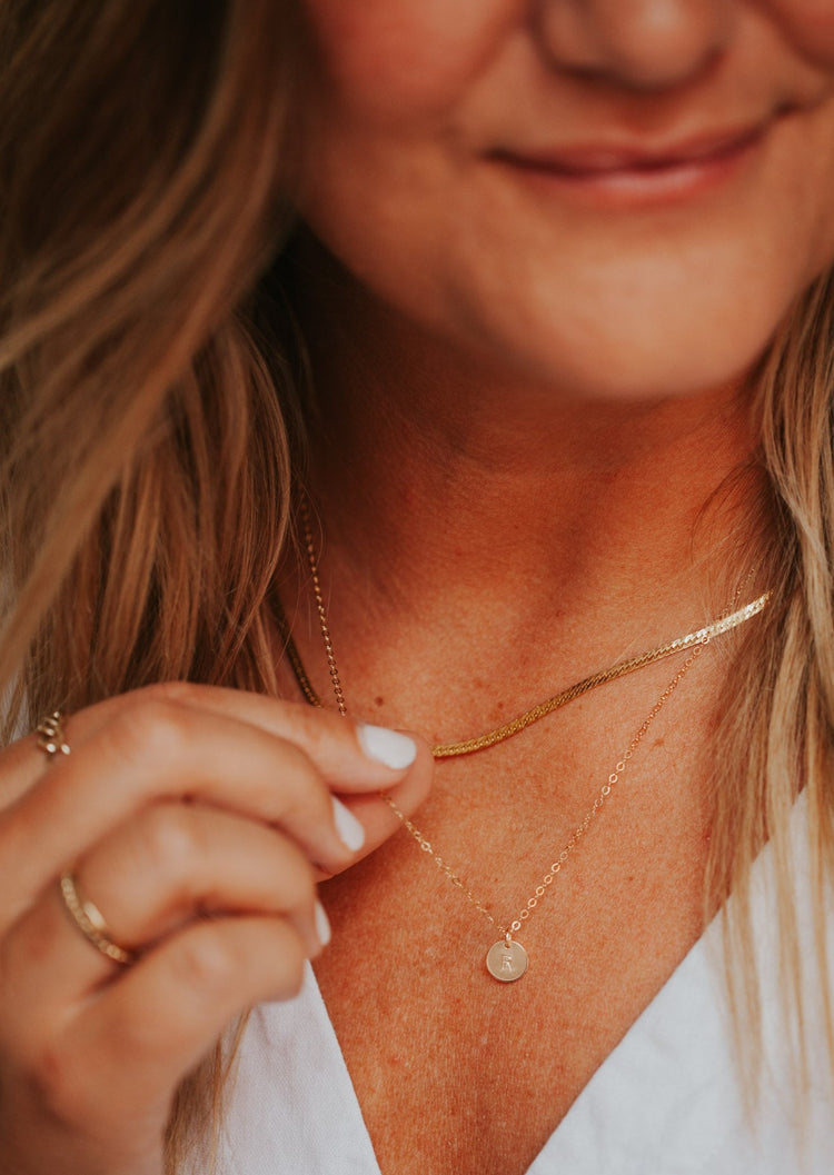 Model is wearing tiny gold initial necklace styled with a herra layering chain by Hello Adorn.