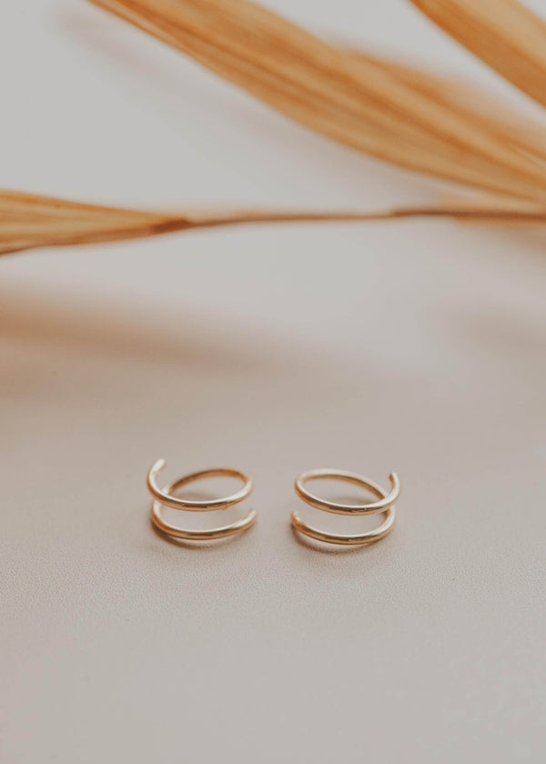 Tiny Twist gold earrings laying flat on a table by Hello Adorn.