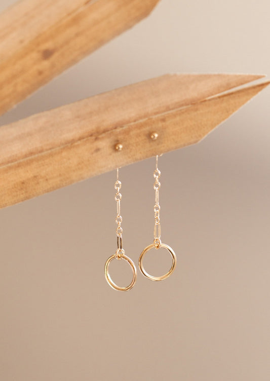 Drop earrings from Hello Adorn in the Monday Backdrop style where a stud earring is attached to a chain drop earring with a circle attached to the end of the chain.