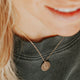 A young model wearing a 14kt Gold Fill necklace with a hand-stamped disc of a feminine silhouette that promotes body positivity..
