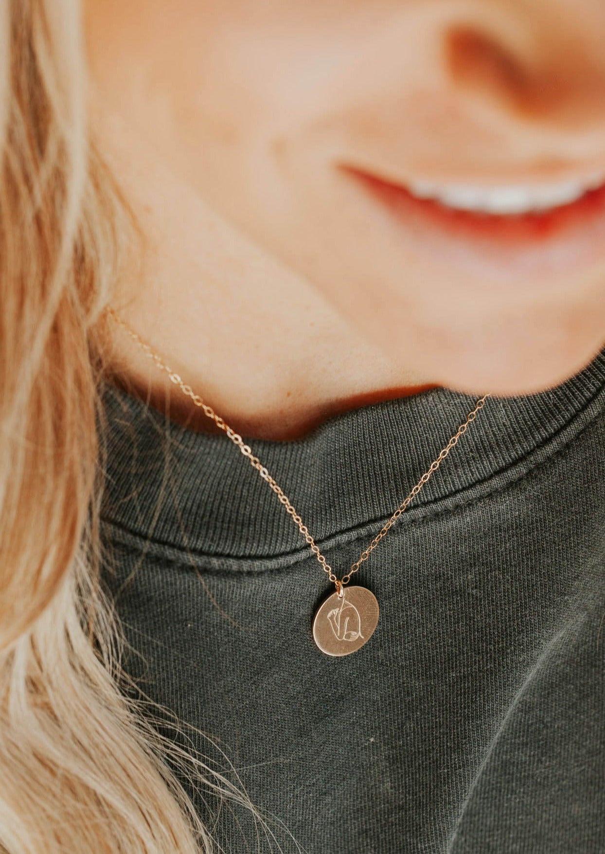 A young model wearing a 14kt Gold Fill necklace with a hand-stamped disc of a feminine silhouette that promotes body positivity..