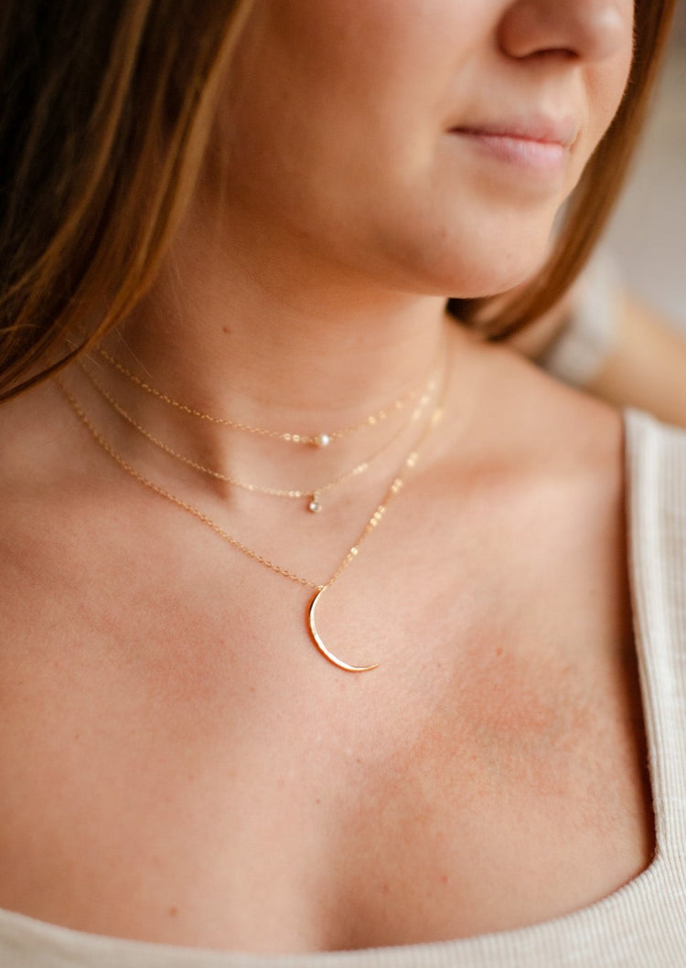 A 3 layered necklace set styled with a mini-moon crescent moon necklace, a stone necklace, and a pearl necklace all handmade by Hello Adorn, pendants and stones are attached to a dainty chain necklace.