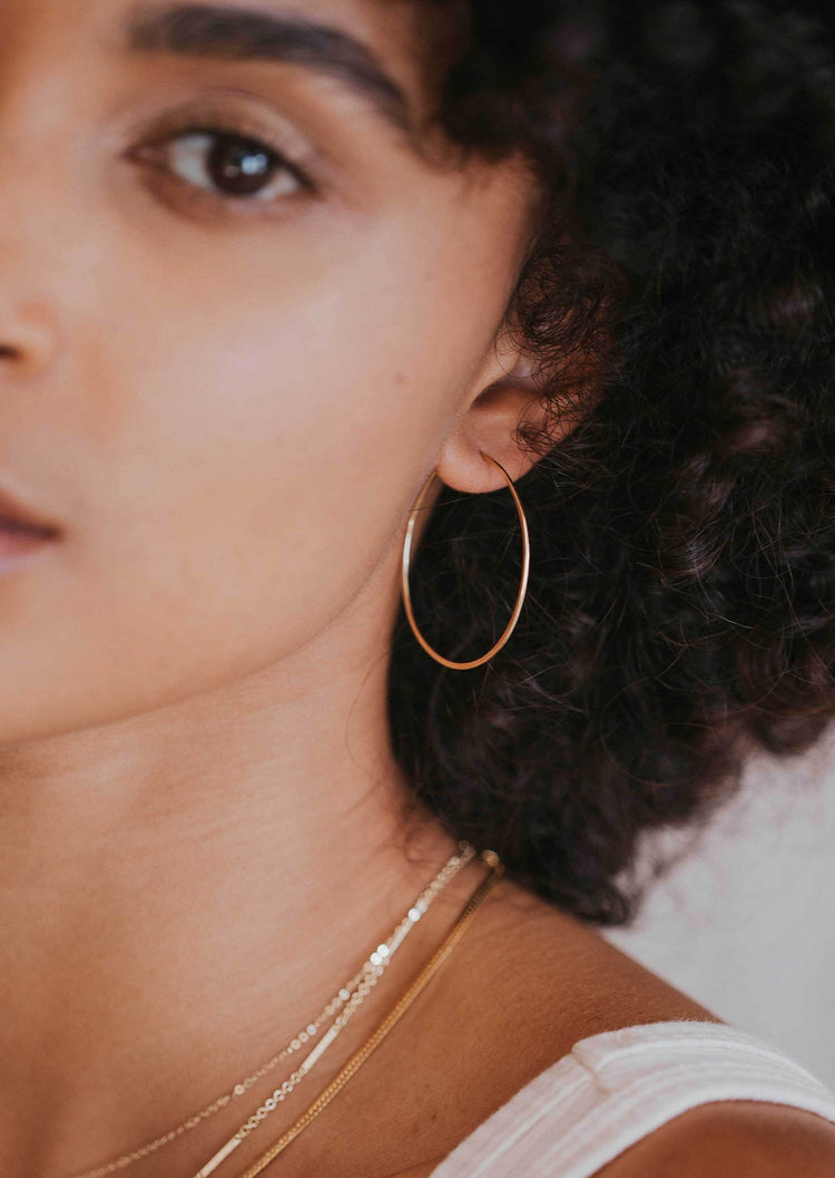 A pair of gold skinny hoops in Cypress Hoops design by Hello Adorn in the largest hoop earring to add to your everyday jewelry collection.
