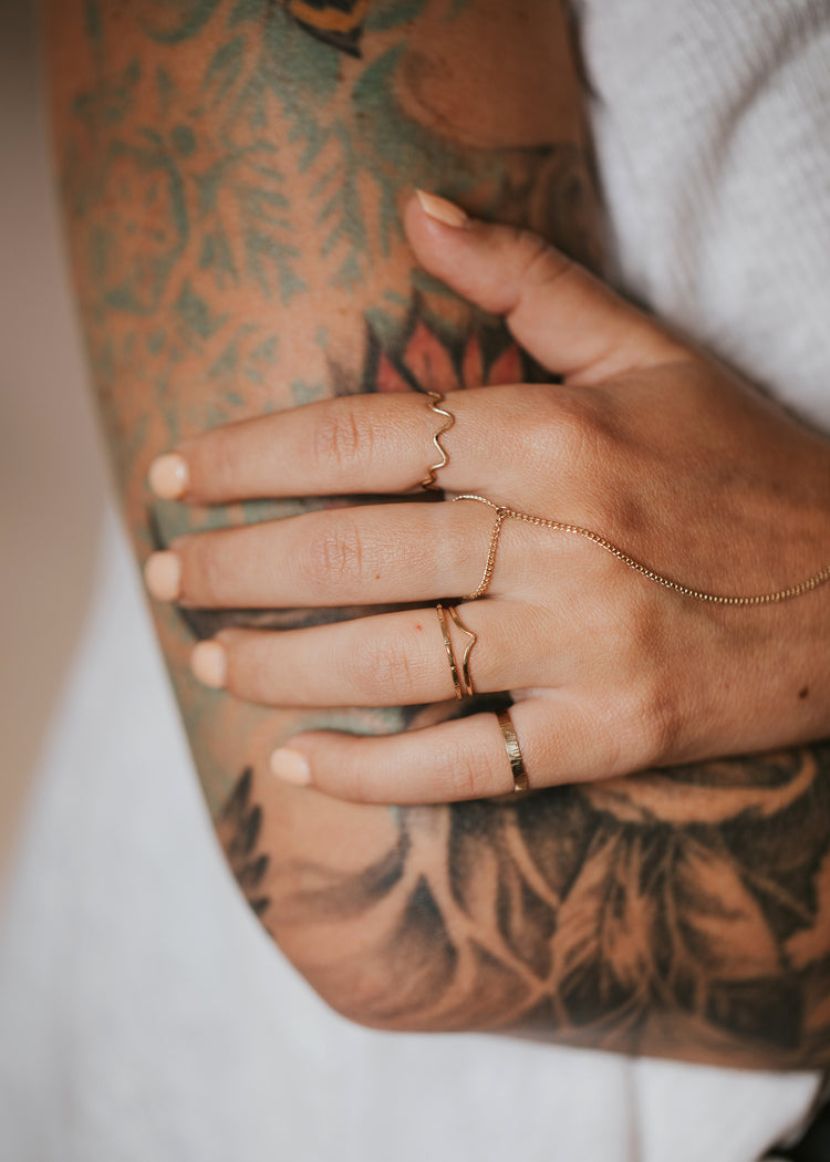 A gold ring stack using a chain and ring to create the demi hand chain, squiggle ring, a thin hammered ring, a wave ring, and a textured ring styled by Hello Adorn.