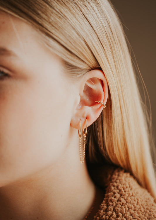 Model wearing multiple earrings featuring a beaded ear cuff and drop hoop earrings.