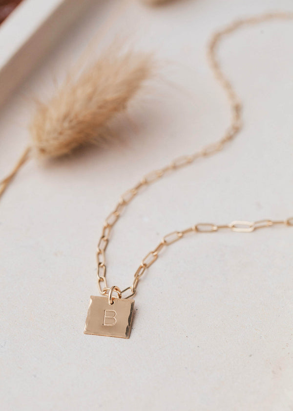 A 14kt Gold Fill square charm necklace with raw, hammered edges and stamped with your favorite initial.