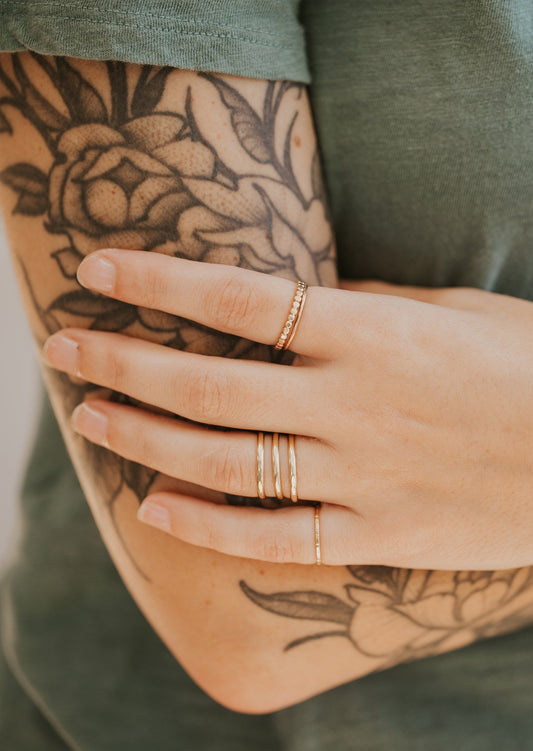 A gold ring stack featuring a statement ring paired with stacking rings in a thin hammered ring, flat thin ring, a beaded ring in Confetti Ring style, and a wrap ring in Triple Wrap Ring style, handmade by Hello Adorn.
