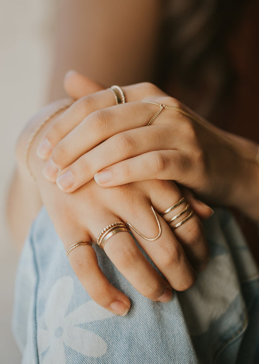 A gold ring stack showing a stackable ring idea using Hello Adorn's stackable ring collection and statement ring collection, this stack features a wire ring hand-shaped and hammered to create a wave ring.