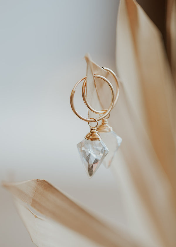 A dagger-shaped, faceted, crystal quartz stone is wire-wrapped and attached to a 14kt Gold Fill endless hoop earring. 