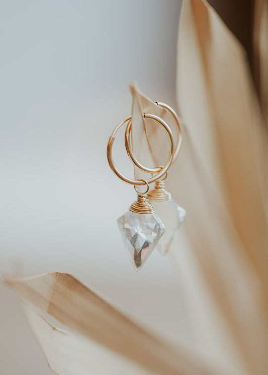 A dagger-shaped, faceted, crystal quartz stone is wire-wrapped and attached to a 14kt Gold Fill endless hoop earring. 