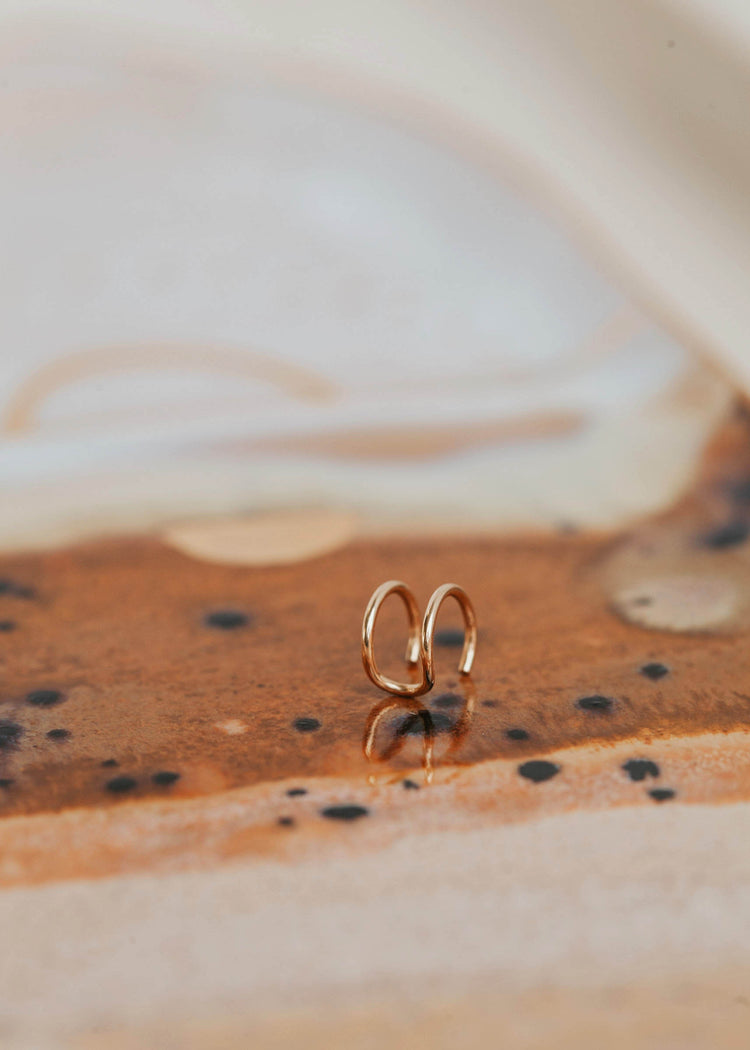 Fake double piercing gold ear cuff by Hello Adorn laying flat on a jewelry tray.