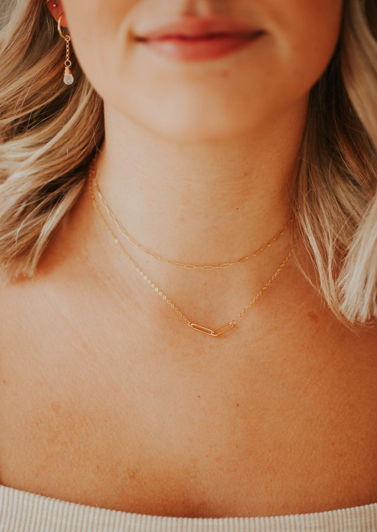 A simple necklace layering idea shown with a paperclip necklace attached to a chain necklace and a chain linked necklace in a choker necklace style from Hello Adorn, paired with a hoop charm earring.