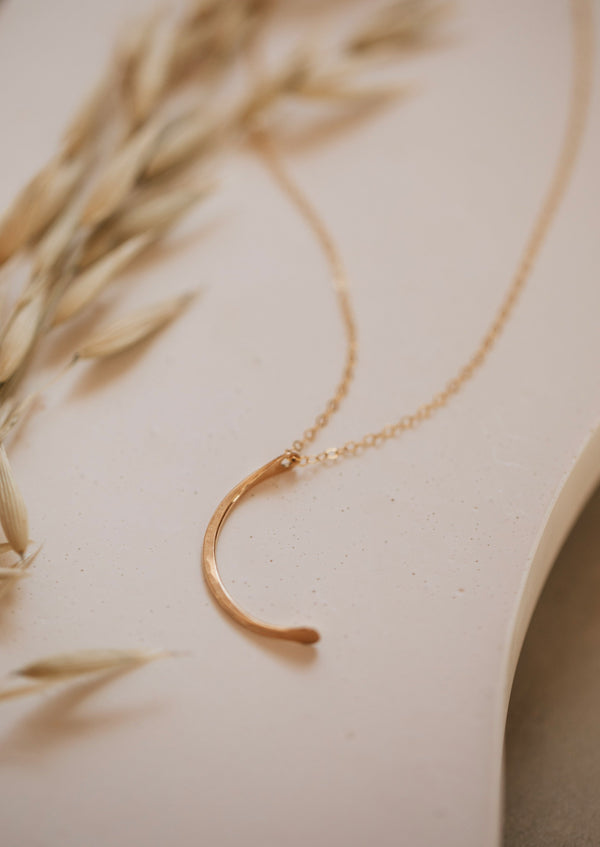 A crescent moon necklace with a hammered gold pendant in a mini-moon shape handmade by Hello Adorn.