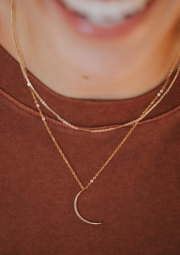 Two layered necklaces in gold, a moon necklace with a mini-moon attached to the bottom of the dainty chain styled with the Mari chain necklace shown in 14k gold fill designed and handmade by Hello Adorn.