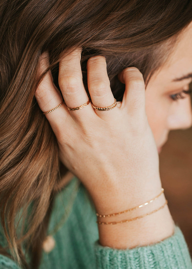 A gold ring stack with 4 stacking rings in a beaded ring style, a braided ring in Nellie Ring style, a hammered ring, and a thin ring paired with a bracelet stack by Hello Adorn.