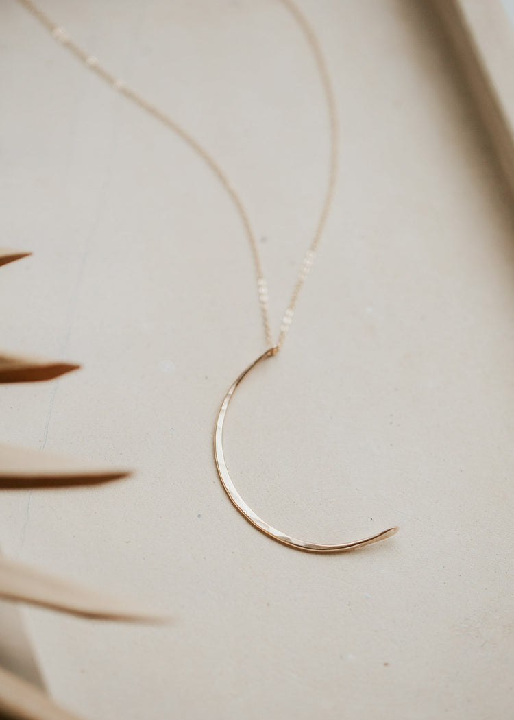 A moon necklace created by Hello Adorn using a hammered gold pendant in the shape of a crescent moon to create a statement necklace to add to a necklace stack.