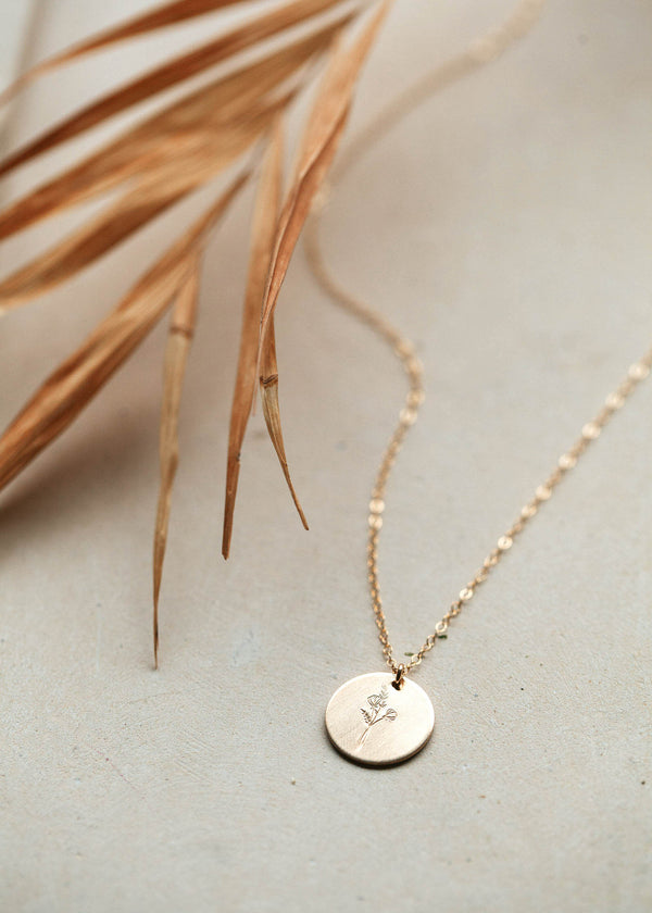 A slightly brushed round disc that is hand-stamped with wildflowers in 14kt Gold FIll.