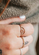 A simple gold ring stack featuring two stacking rings in the confetti ring style paired with two statement rings in a chain ring style and a ring-shaped as a rainbow in the Raye Ring design by Hello Adorn.
