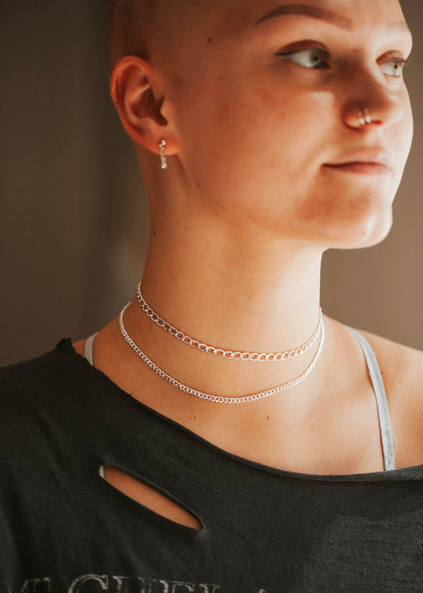 A young model layering two Sterling Silver flat curb chain necklaces.