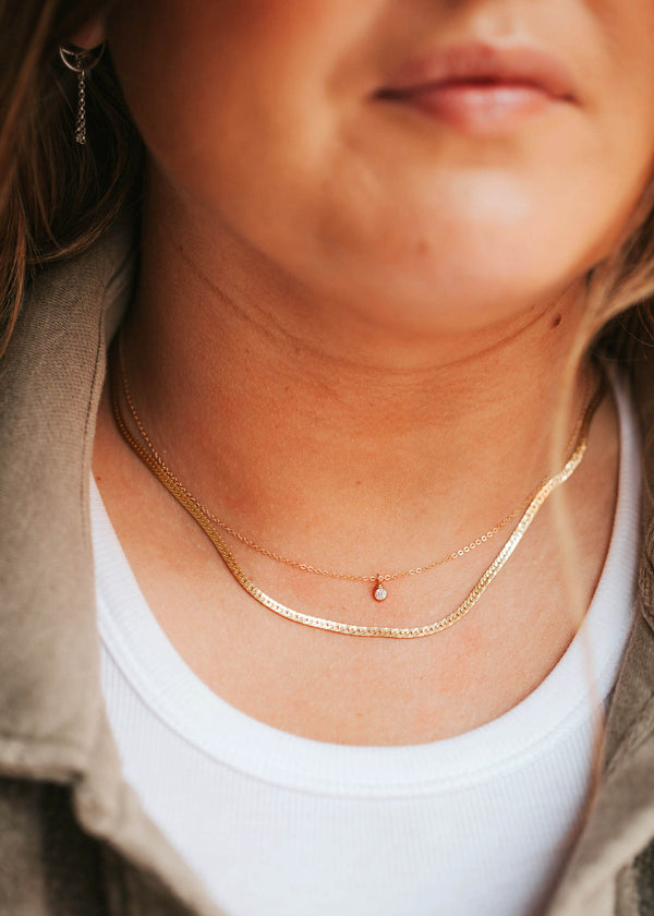 A solitaire bezel necklace suspended from a delicate 14kt Gold Fill chain layered with a thin herra chain.