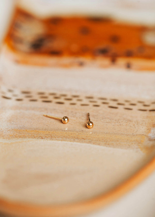 A close up look at a pair of gold ball stud earrings made for daily wear earrings shown in 14k gold fill by Hello Adorn.