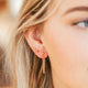 A model showing off her earring stack styled with a gold ball earring, twist earrings, and an earring with a chain shown in 14k gold fill by Hello Adorn.