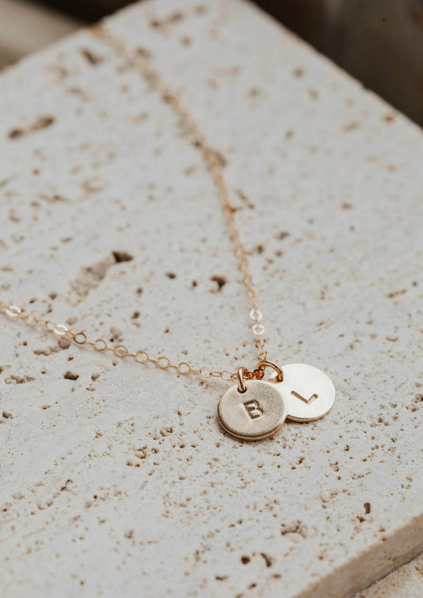 Gold stamped jewelry attached to a gold initial necklace by Hello Adorn laying flat.